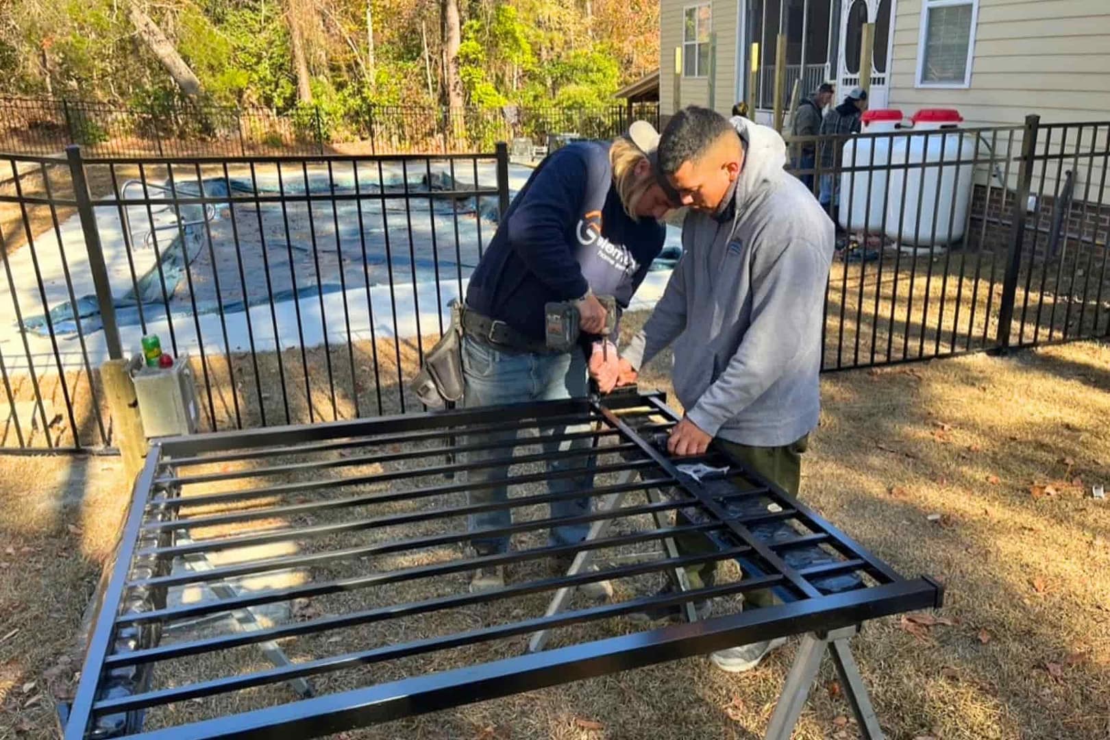 Two workers building an aluminum fence around a backyard with a pool.